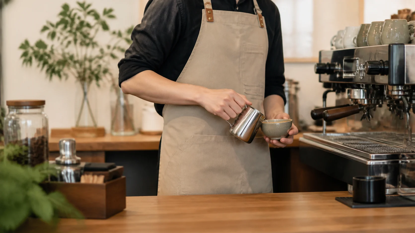 Barista mặc tạp dề cafe màu trung tính trong quầy pha chế hiện đại